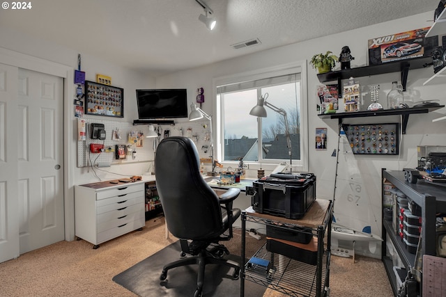 carpeted office featuring a textured ceiling and track lighting