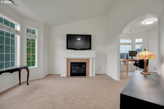 living room with a healthy amount of sunlight, light colored carpet, a tile fireplace, and vaulted ceiling