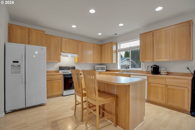 kitchen with light wood-type flooring, light brown cabinetry, white appliances, and a kitchen breakfast bar