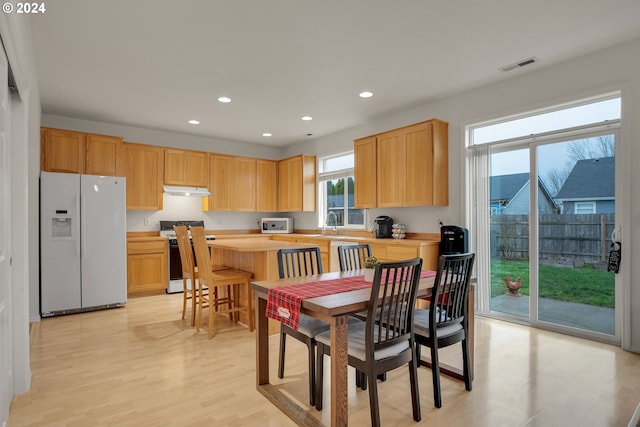 kitchen featuring stove, light wood-type flooring, white fridge with ice dispenser, and light brown cabinetry