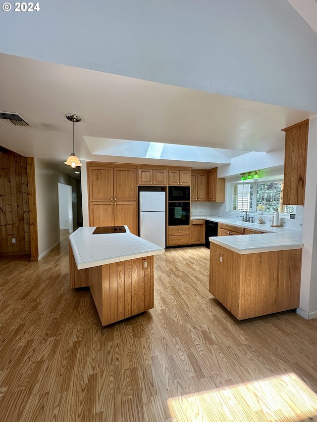 kitchen featuring kitchen peninsula, pendant lighting, light hardwood / wood-style flooring, and black appliances