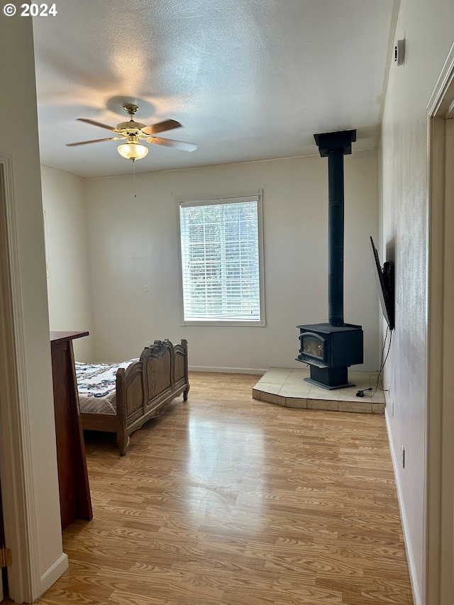 living room with a textured ceiling, light wood-type flooring, a wood stove, and ceiling fan