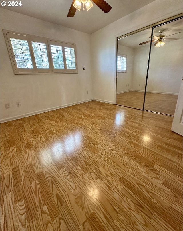 unfurnished bedroom featuring ceiling fan, light hardwood / wood-style floors, multiple windows, and a closet