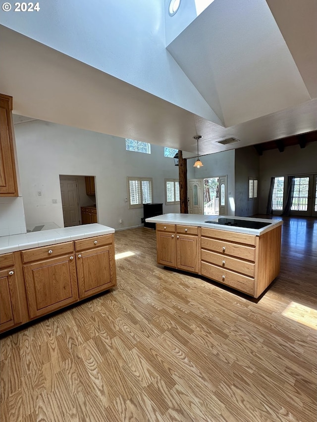 kitchen featuring cooktop, high vaulted ceiling, kitchen peninsula, light hardwood / wood-style floors, and decorative light fixtures