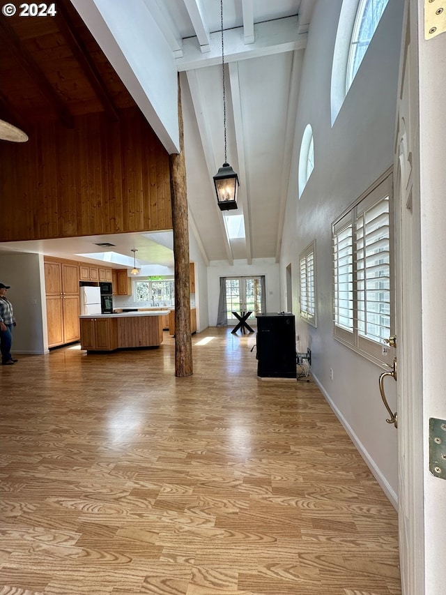 interior space featuring beam ceiling, high vaulted ceiling, decorative columns, and light hardwood / wood-style flooring