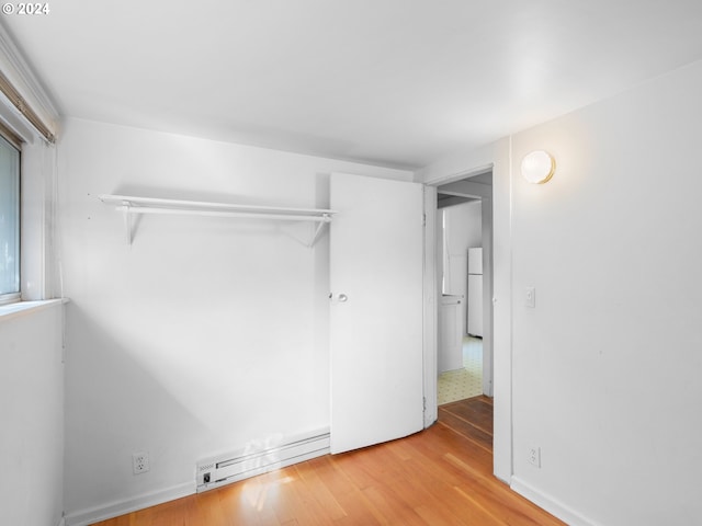 unfurnished bedroom with a closet, hardwood / wood-style flooring, a baseboard heating unit, and white refrigerator