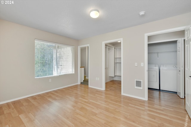 unfurnished bedroom featuring washing machine and clothes dryer, a spacious closet, light hardwood / wood-style flooring, and a textured ceiling