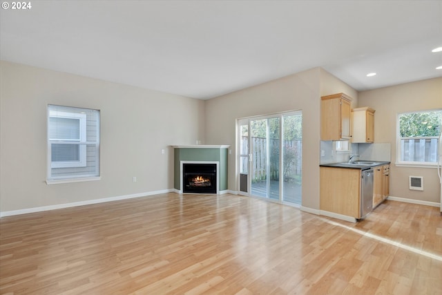 kitchen featuring decorative backsplash, light brown cabinetry, light wood-type flooring, stainless steel dishwasher, and sink