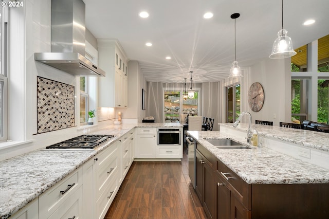 kitchen featuring pendant lighting, white cabinets, wall chimney range hood, sink, and appliances with stainless steel finishes