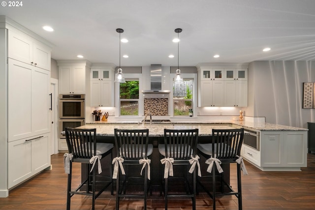 kitchen featuring wall chimney exhaust hood, white cabinetry, light stone countertops, and stainless steel appliances