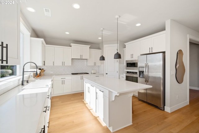 kitchen with appliances with stainless steel finishes, hanging light fixtures, a center island, and light hardwood / wood-style flooring