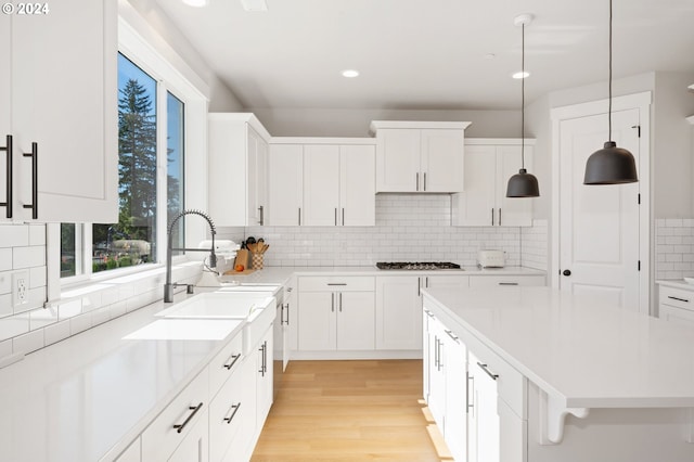 kitchen with light hardwood / wood-style floors, a center island, white cabinetry, hanging light fixtures, and backsplash