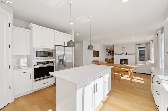 kitchen featuring light wood-type flooring, white cabinets, hanging light fixtures, a brick fireplace, and appliances with stainless steel finishes