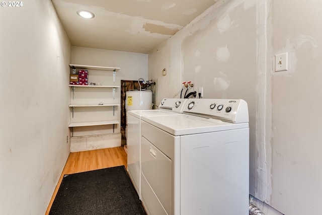 laundry room featuring water heater, washing machine and clothes dryer, and light wood-type flooring