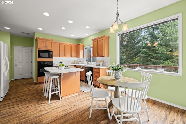 kitchen featuring pendant lighting, tasteful backsplash, light hardwood / wood-style flooring, black appliances, and a center island