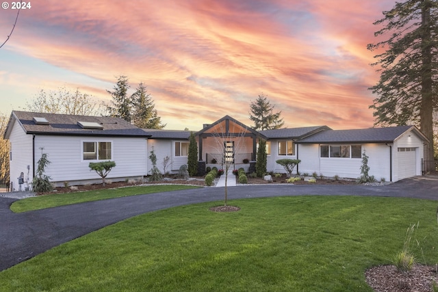 ranch-style house featuring a garage, solar panels, and a lawn