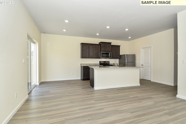 kitchen with dark brown cabinets, light wood-style flooring, appliances with stainless steel finishes, and a kitchen island with sink