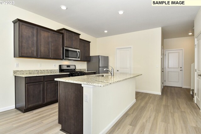 kitchen with light wood finished floors, a sink, dark brown cabinets, appliances with stainless steel finishes, and a kitchen island with sink