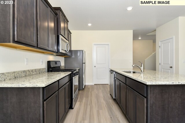 kitchen featuring dark brown cabinets, a center island with sink, light wood-style flooring, stainless steel appliances, and a sink