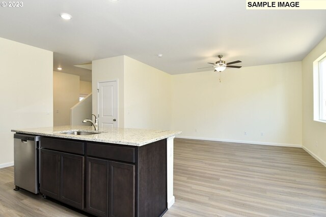 kitchen with light wood-type flooring, an island with sink, a sink, baseboards, and dishwasher