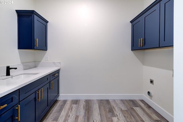 laundry area with electric dryer hookup, cabinets, sink, and light hardwood / wood-style flooring