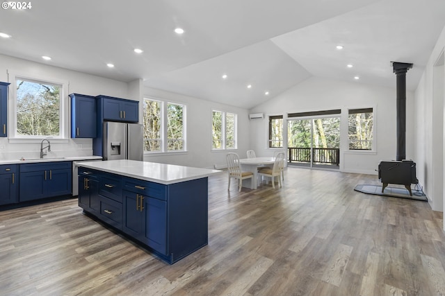 kitchen with stainless steel fridge with ice dispenser, tasteful backsplash, light hardwood / wood-style flooring, a wood stove, and sink