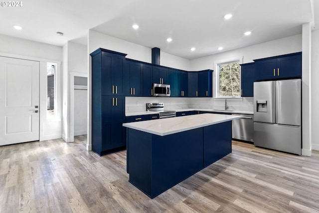 kitchen with appliances with stainless steel finishes, a center island, sink, light hardwood / wood-style flooring, and light stone countertops