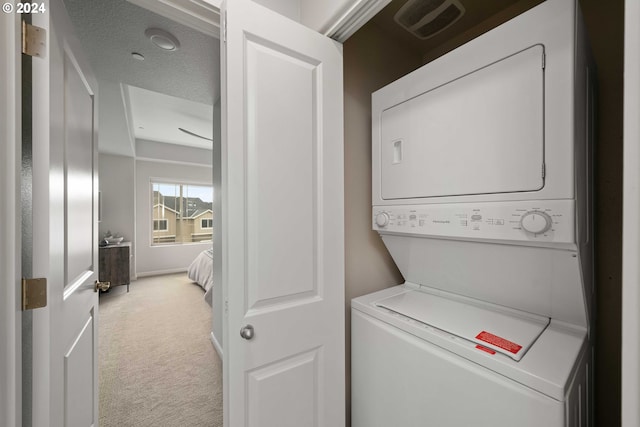 laundry room with light carpet, stacked washer and clothes dryer, and a textured ceiling