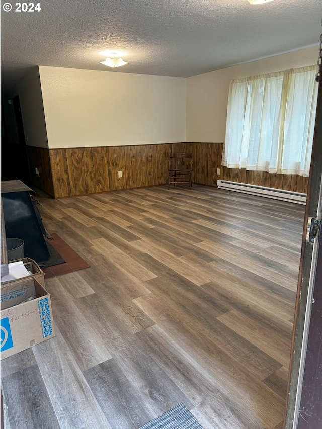 spare room with baseboard heating, a textured ceiling, hardwood / wood-style flooring, and wooden walls