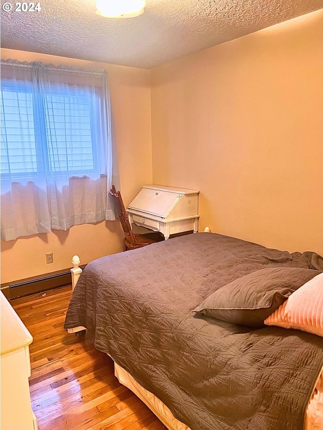 bedroom featuring a textured ceiling, light hardwood / wood-style flooring, and baseboard heating