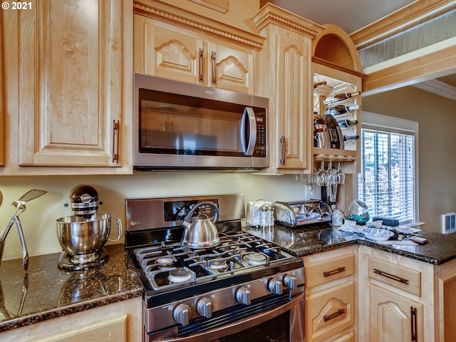 kitchen with dark stone countertops, light brown cabinetry, ornamental molding, and appliances with stainless steel finishes