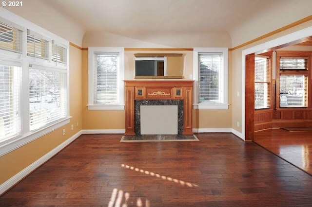 unfurnished living room with dark wood-type flooring, a high end fireplace, and a healthy amount of sunlight