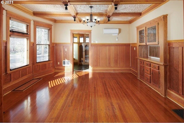 unfurnished dining area with coffered ceiling, a wall mounted AC, beamed ceiling, hardwood / wood-style floors, and a chandelier