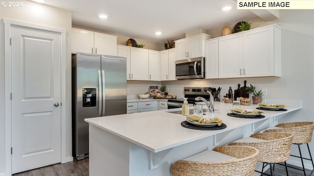 kitchen with stainless steel appliances, sink, wood-type flooring, white cabinetry, and a breakfast bar area