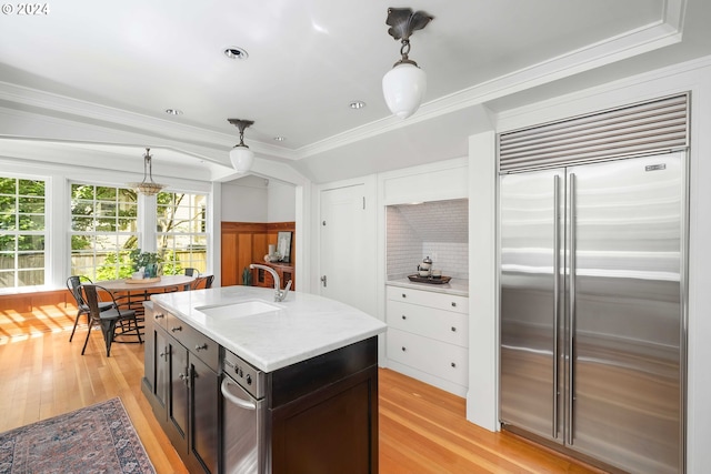 kitchen with sink, hanging light fixtures, built in fridge, ornamental molding, and light hardwood / wood-style flooring