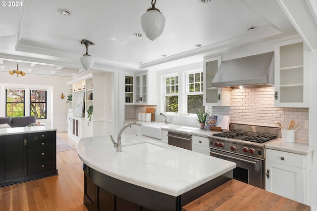 kitchen with decorative light fixtures, appliances with stainless steel finishes, backsplash, light hardwood / wood-style floors, and wall chimney exhaust hood