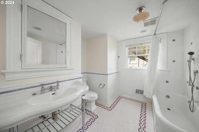 bathroom featuring tile floors, tiled shower / bath, toilet, and tile walls