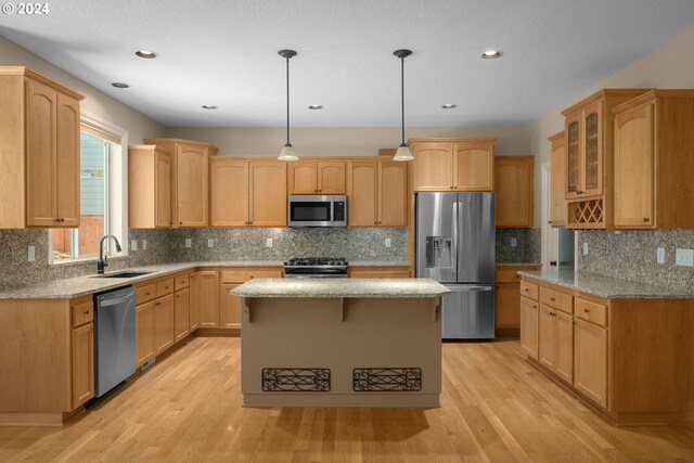 kitchen with light stone counters, stainless steel appliances, glass insert cabinets, a sink, and light wood-type flooring