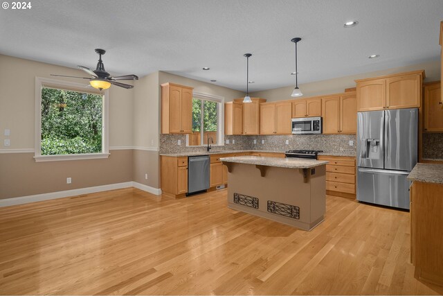 kitchen featuring sink, a center island, pendant lighting, light wood-type flooring, and stainless steel appliances