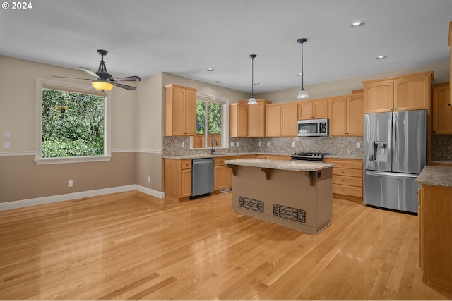 kitchen featuring a sink, appliances with stainless steel finishes, backsplash, a center island, and light wood finished floors