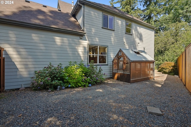 rear view of property featuring a greenhouse, fence, an outbuilding, and roof with shingles