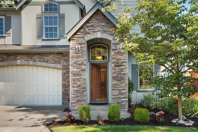 view of exterior entry featuring an attached garage, stone siding, concrete driveway, and stucco siding