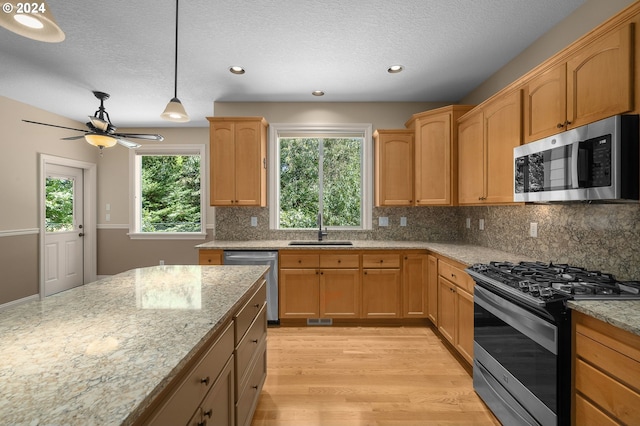 kitchen with light wood-type flooring, appliances with stainless steel finishes, sink, and light stone counters