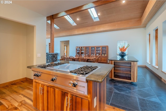 kitchen featuring a center island, dark stone counters, a skylight, wood ceiling, and stainless steel gas cooktop