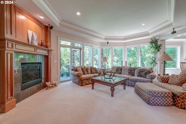 carpeted living room featuring a tile fireplace, a tray ceiling, and crown molding