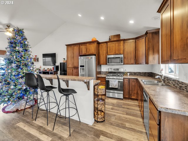566 N 11th St, Aumsville, OR 97325 - kitchen with appliances with stainless steel finishes, a sink, a kitchen breakfast bar, light wood-style floors, and brown cabinets