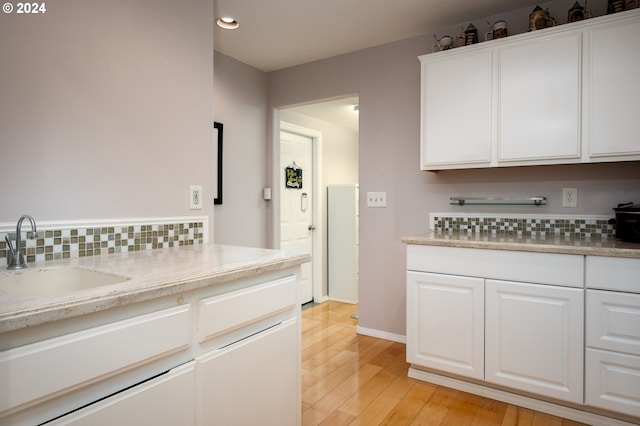 kitchen with tasteful backsplash, light wood-type flooring, sink, and white cabinets