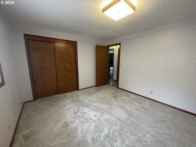 unfurnished bedroom featuring a closet, baseboards, a textured ceiling, and light colored carpet