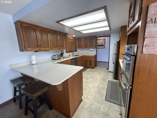 kitchen featuring stainless steel appliances, a peninsula, a breakfast bar area, brown cabinetry, and light countertops