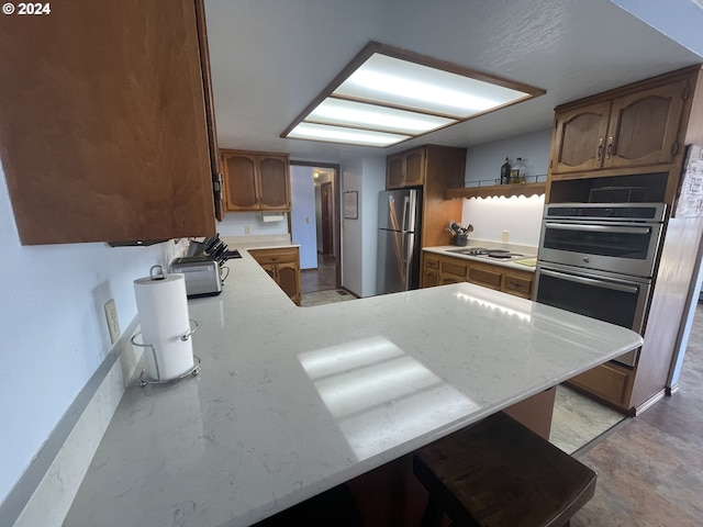 kitchen featuring brown cabinetry, appliances with stainless steel finishes, and a peninsula